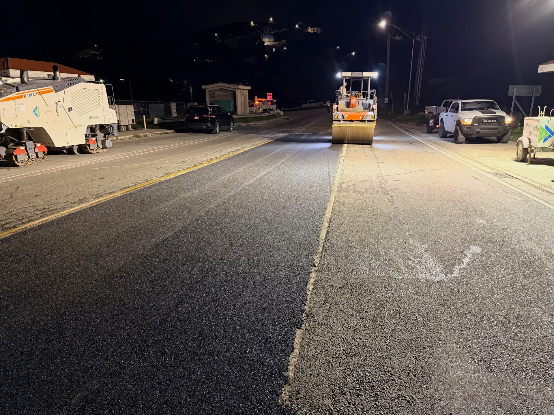 Nighttime asphalt paving operation with paving equipment and rollers on a road project